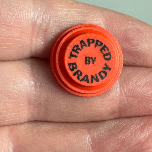 Vtg “Trapped by Brandy” Novelty Clay Target Pin – Funny Orange Lapel Badge